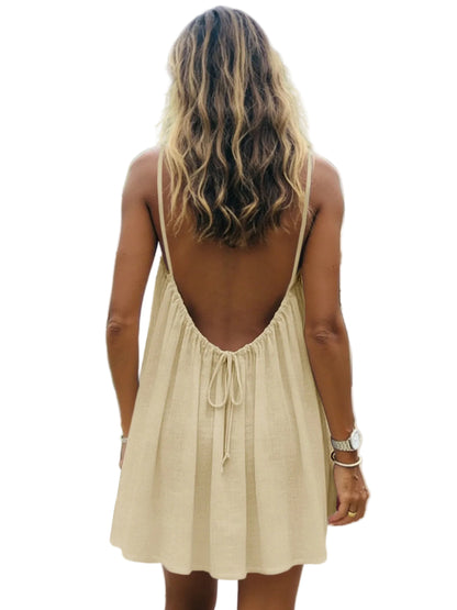 Woman wearing a beige dress with an open back, standing outdoors with greenery in the background.